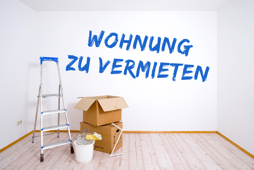 Leeres Zimmer mit Kartons und Leiter mit Wandschrift Wohnung zu vermieten